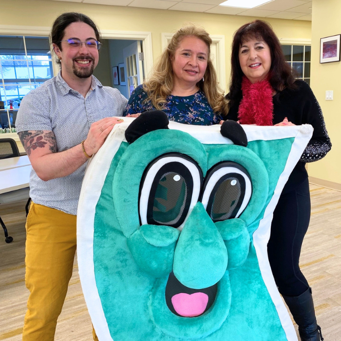 Three financial wellness coaches pose with a smiling dollar bill costume character