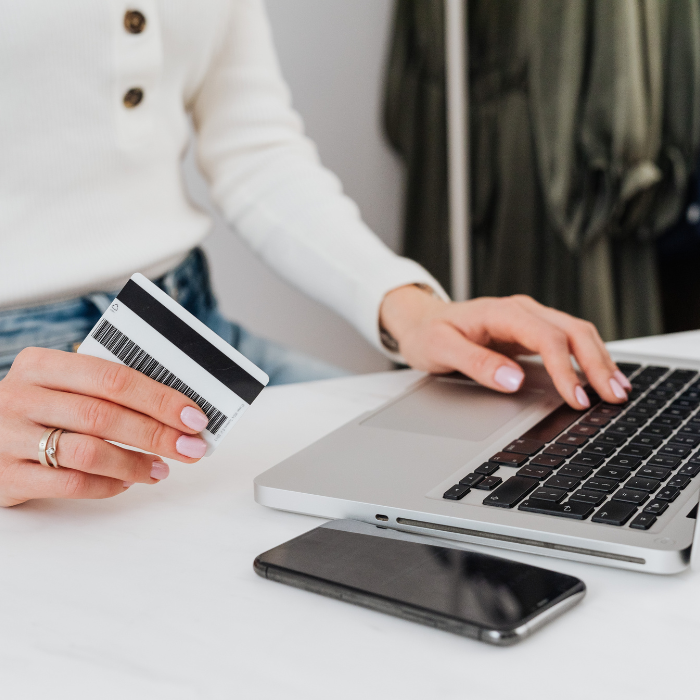 a woman's hand hold a credit card while typing on a laptop with a phone near by